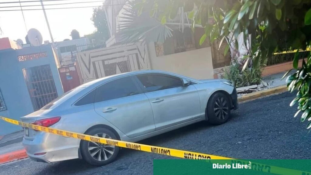 Vehículo gris de la víctima rodeado por cinta policial en una calle de Santo Domingo