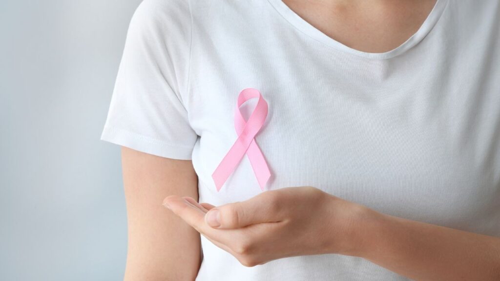 Una mujer con camiseta blanca lleva prendido en el pecho un lazo rosado, símbolo de la lucha contra el cáncer de mama