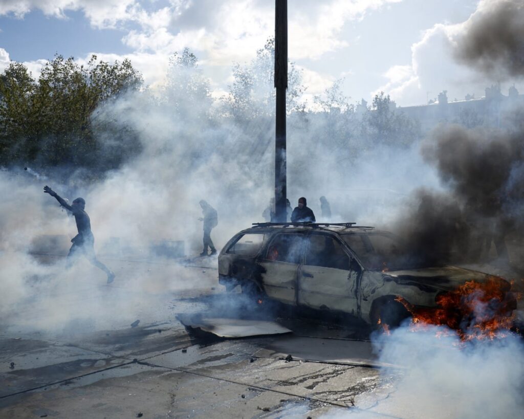 Protestas masivas en Francia terminan con saqueos y más de 400 detenidos; Macron promete castigar a los violentos Manifestantes encapuchados entre nubes de gas lacrimógeno junto a un automóvil en llamas durante las protestas del sábado 17 de octubre en Francia; uno de ellos lanza un objeto